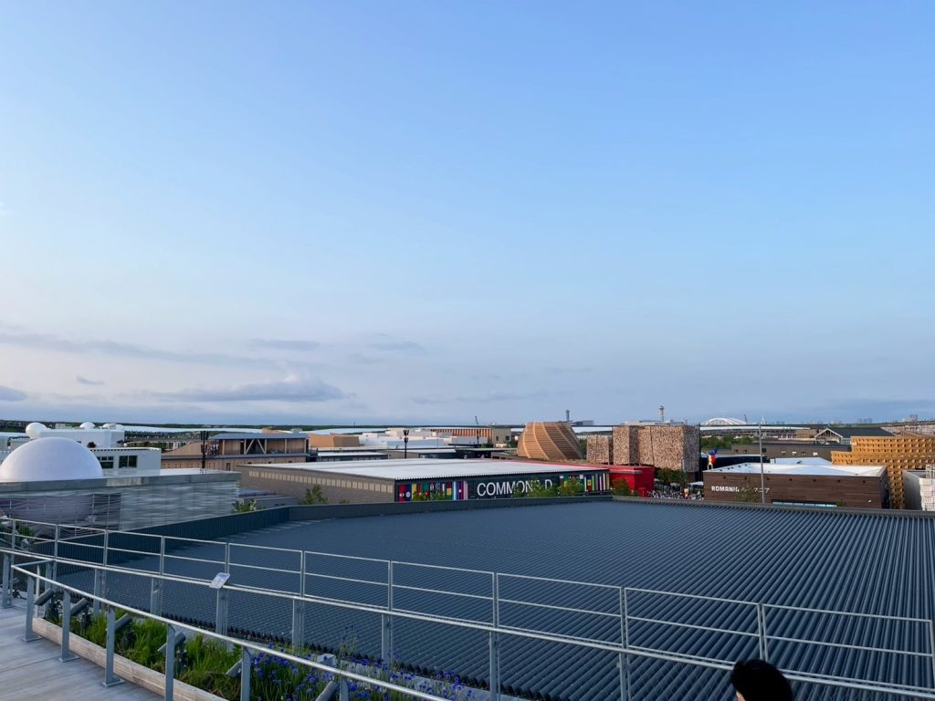 大阪・関西万博の木組み建築のディテールが青空を背景に印象的に映える構図。日本の伝統建築技術と現代建築の融合を視覚的に伝える。